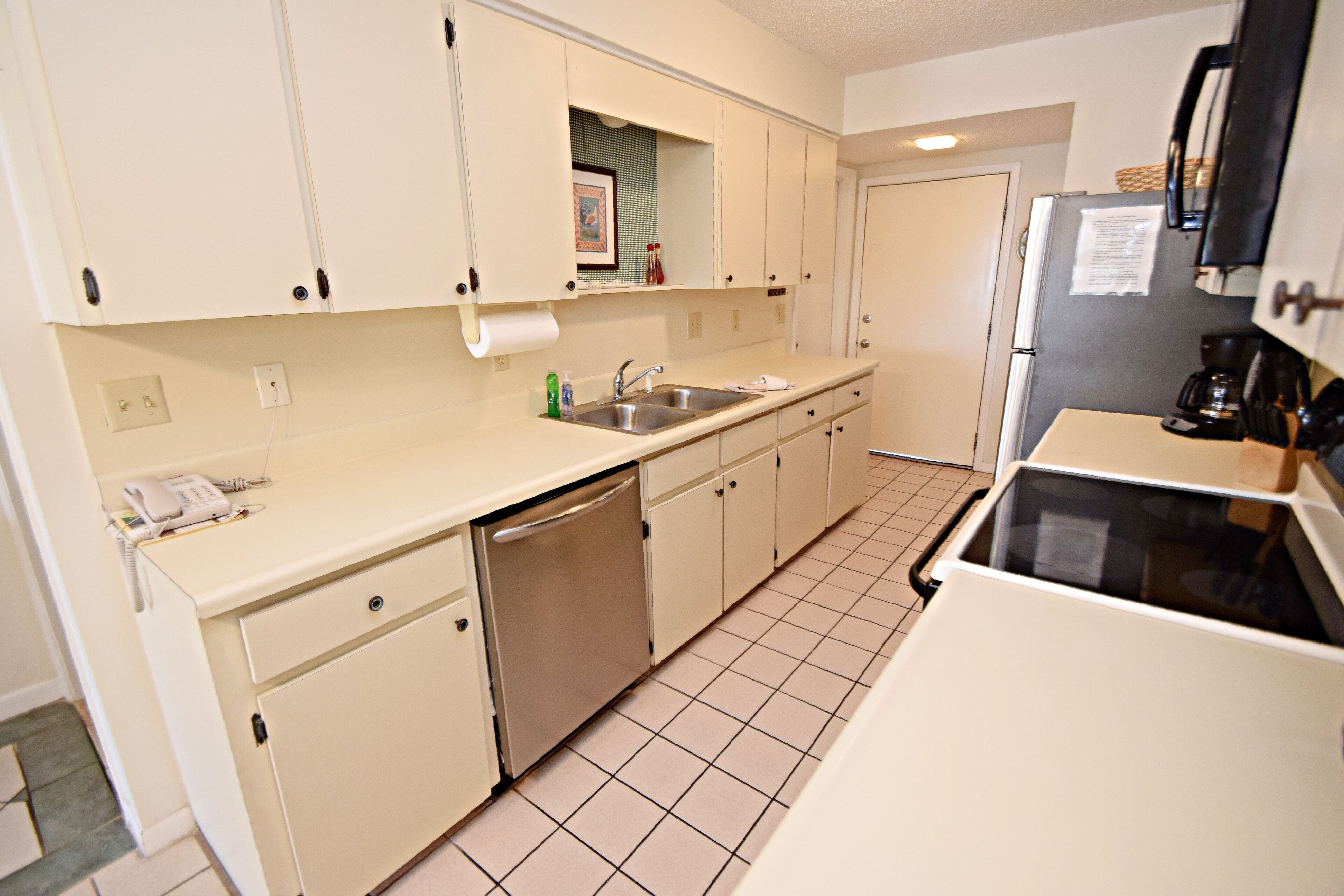 A compact kitchen with white cabinets, a sink, a dishwasher, and a refrigerator.