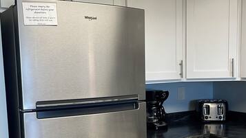 Een roestvrijstalen Whirlpool koelkast in een keuken met witte kasten en een zwart aanrecht.