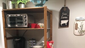 A kitchen with a built-in microwave, toaster, and coffee maker. There are shelves with kitchenware and a red towel hanging. - Quiet Cottage in the Country (Cove)