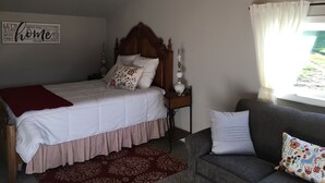 A bedroom with a bed, a bedside table, a lamp, a window with curtains, and a wall with a motivational quote. - Quiet Cottage in the Country (Cove)