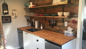 A compact kitchen with wooden shelves, a sink, and a dishwasher. - Quiet Cottage in the Country (Cove)