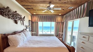 Une chambre avec un grand lit, un ventilateur de plafond et une vue sur la plage.