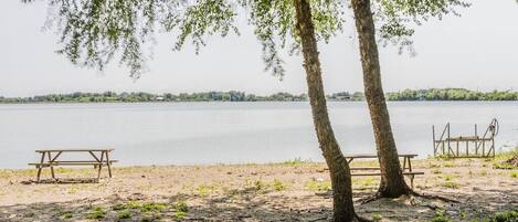 Un espace de pique-nique au bord du lac, équipé de deux tables et de deux bancs en bois, entouré d’arbres et bordé d’une étendue d’eau calme.