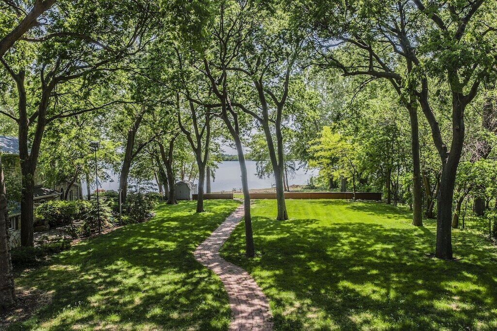 A pathway leading through a lush garden with trees and a view of a body of water.