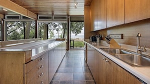 A modern kitchen with wooden cabinets, stainless steel countertops, and a view of the outdoors. - GLASS HOUSE 5 BR Private Lake Erie Beach Great for Summer, Fall, Winter (Sandusky)