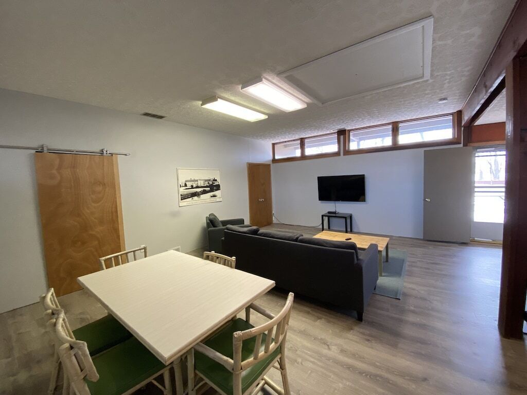 A room with a white table and chairs, a dark sofa, a TV on a stand, and a wooden door.