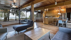 A spacious living area with a large sofa, a dining table, and a kitchen area with wooden cabinets and a stainless steel refrigerator. - GLASS HOUSE 5 BR Private Lake Erie Beach Great for Summer, Fall, Winter (Sandusky)