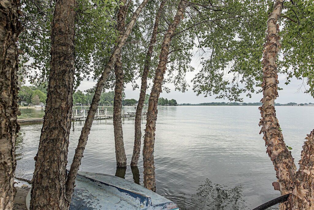 A calm lake with trees in the foreground and a dock extending into the water.