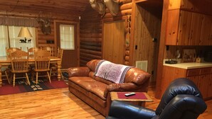A log cabin interior with a leather sofa, a blue armchair, wooden dining table, and chairs.