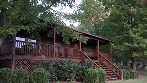A wooden cabin with a porch, stairs, and a fenced yard.