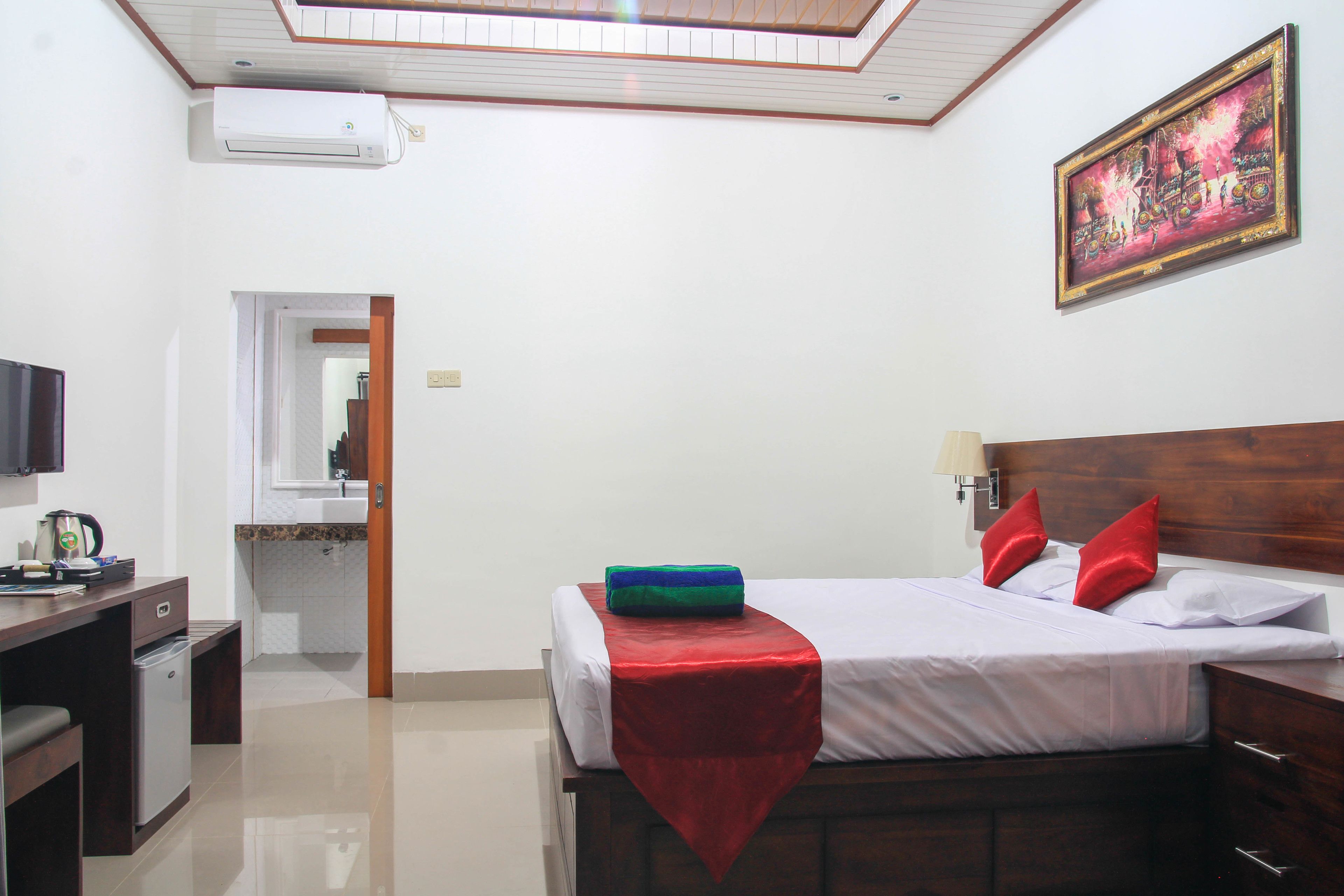 A hotel room with a bed, a desk with a television, a small refrigerator, and a bathroom visible through an open door.