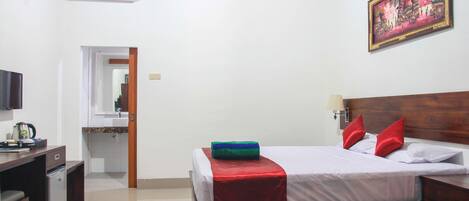 A hotel room with a bed, a desk with a television, a small refrigerator, and a bathroom visible through an open door.