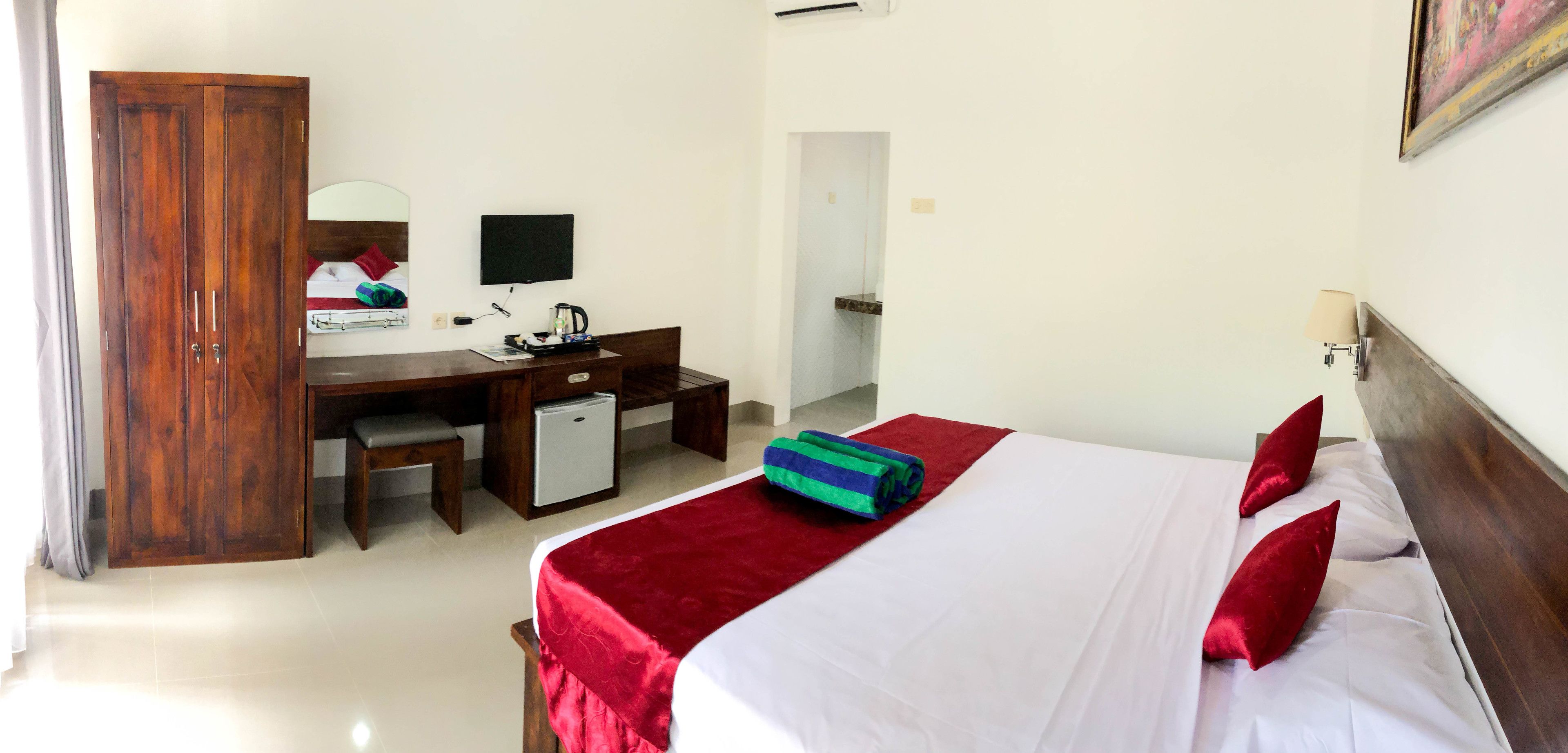 A hotel room with a bed, a desk with a computer, a small fridge, and a wardrobe.