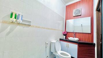 Un baño con inodoro, lavamanos y espejo. Hay dispensadores de jabón de manos en la pared.