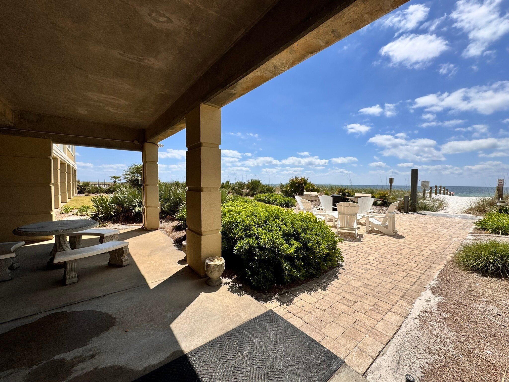A covered outdoor area with a patio, seating, and a view of the beach.