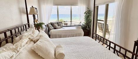 Een slaapkamer met een groot bed, een balkon met uitzicht op de oceaan en een plafondventilator.