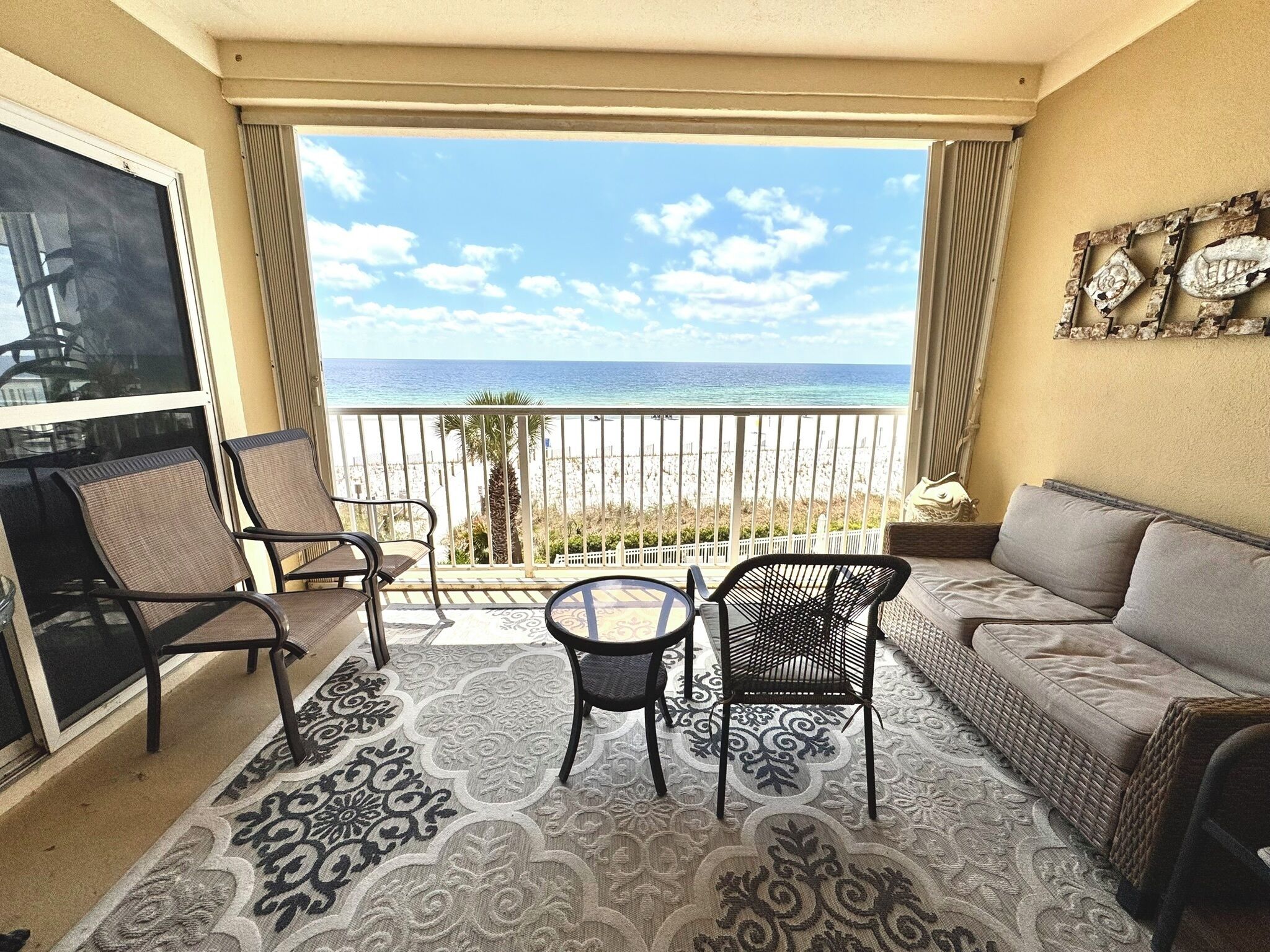 A balcony with a view of the beach, furnished with two chairs, a table, and a sofa.