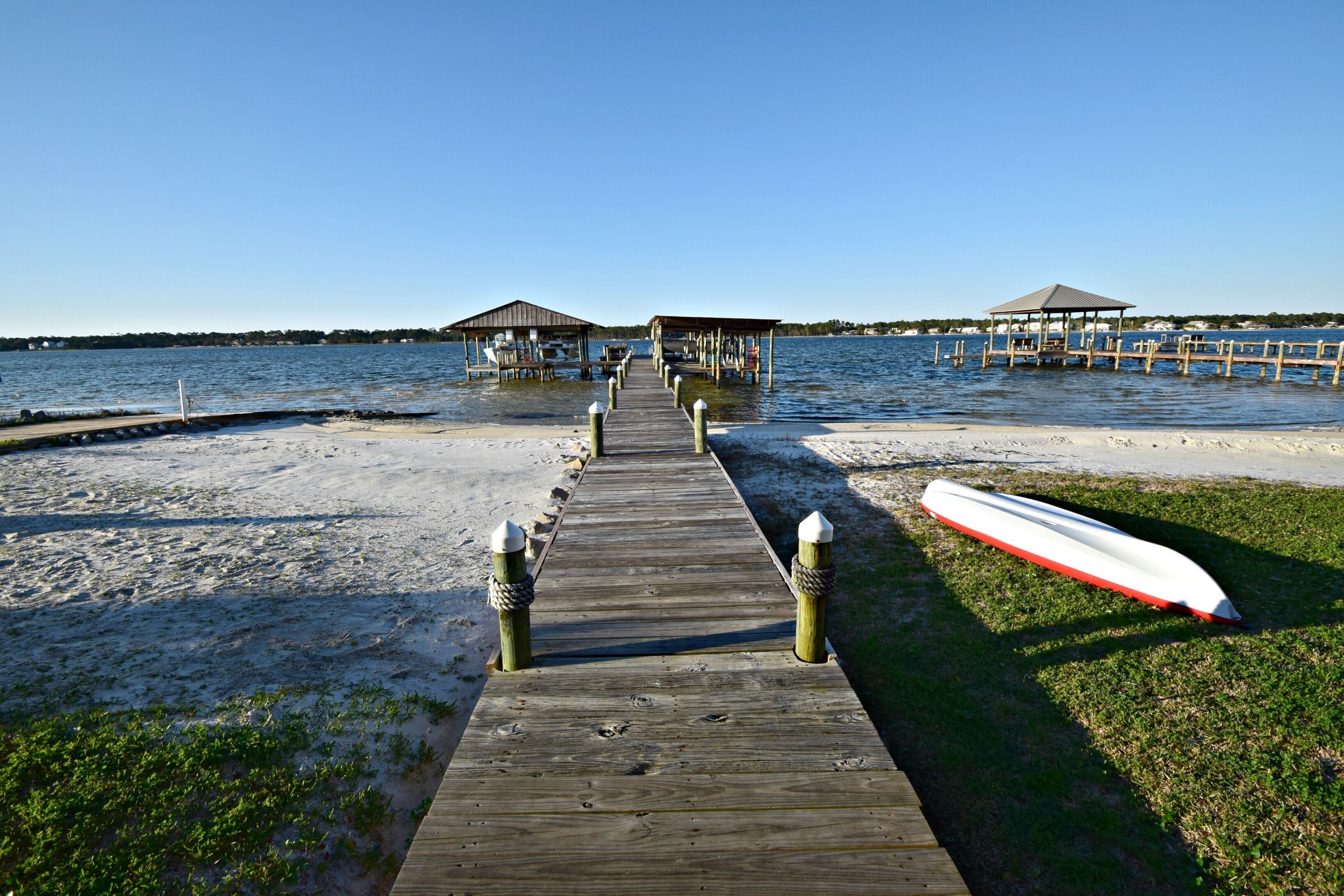 A wooden pier leading to two covered structures by the water.