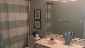 Ein Badezimmer mit gestreifter Duschvorhang, Toilette, Waschbecken mit Spiegel und zwei gerahmten Bildern an der Wand.