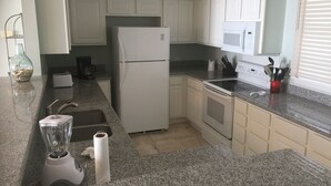 Eine Küche mit weißen Schränken, einem Kühlschrank, einem Herd, einer Spüle und einer Arbeitsplatte mit einem Mixer und einer roten Tasse mit Besteck.