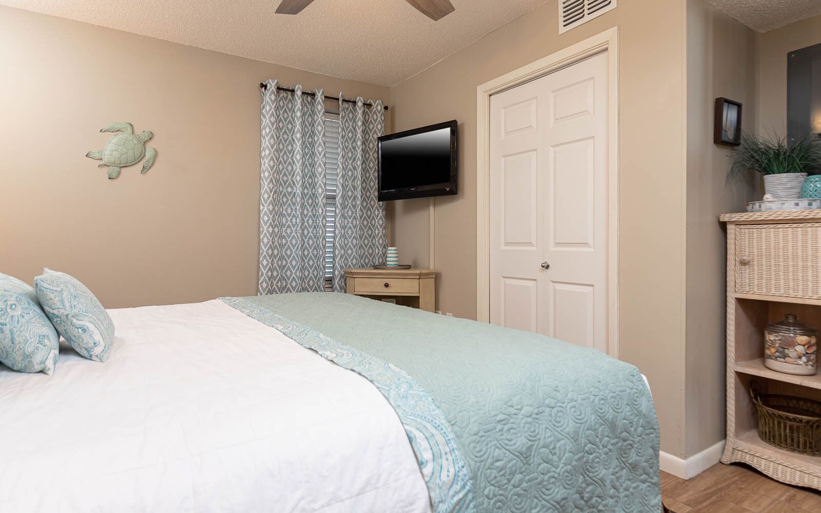 A bedroom with a bed, a television, a door, and a shelf with decorative items.