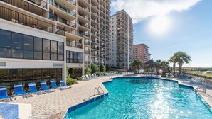 Una piscina con lettini, un edificio con diversi balconi e un cielo sereno.