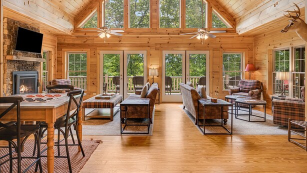 A spacious wooden cabin with a high ceiling, large windows, and a fireplace.