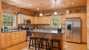 A wooden cabin-style kitchen with a central island, bar stools, a stainless steel refrigerator, and wooden cabinets.