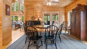 A wooden cabin interior with a dining area, a ceiling fan, and a view of the outdoors.