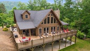 A two-story log cabin with a deck, large windows, and a stone chimney.