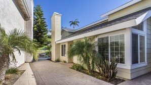 Une maison moderne avec un patio dallé, des palmiers et un ciel d’un bleu éclatant.
