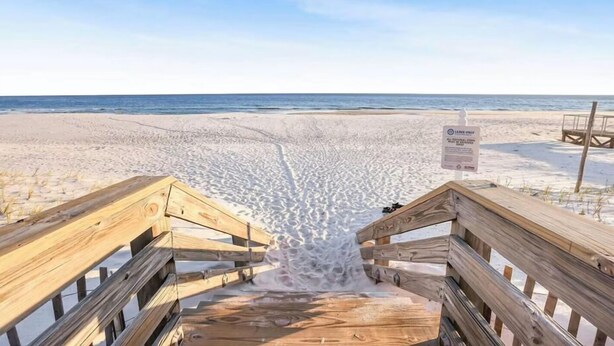 Ein Holzsteg führt zu einem Strand, an dem ein Schild mit dem Hinweis 'Müll nicht mitnehmen' steht.