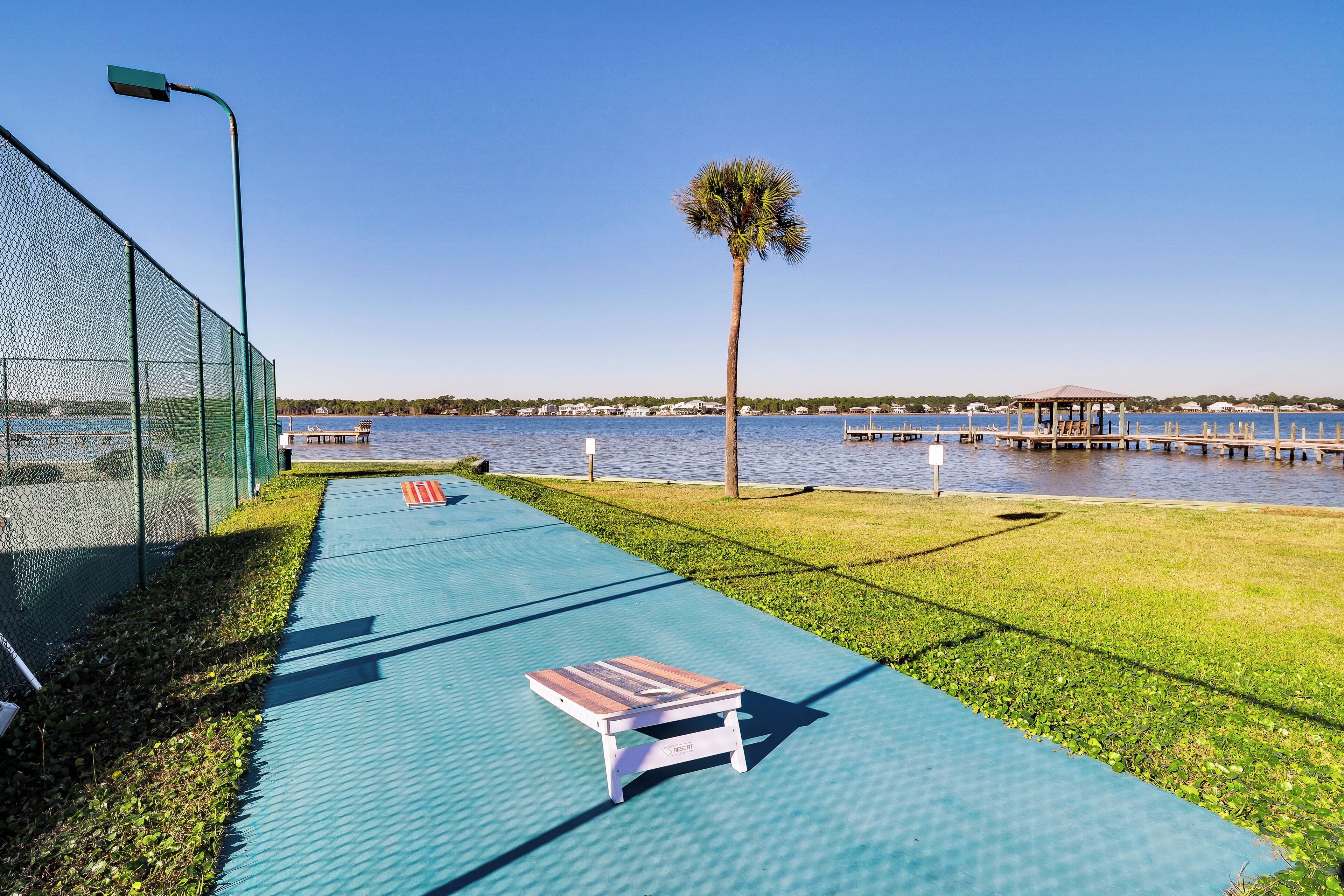 A waterfront walkway with a bench, a palm tree, and a dock in the background.