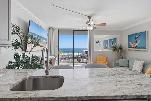 A modern kitchen with a large island, a built-in sink, and a view of the ocean through a sliding glass door.
