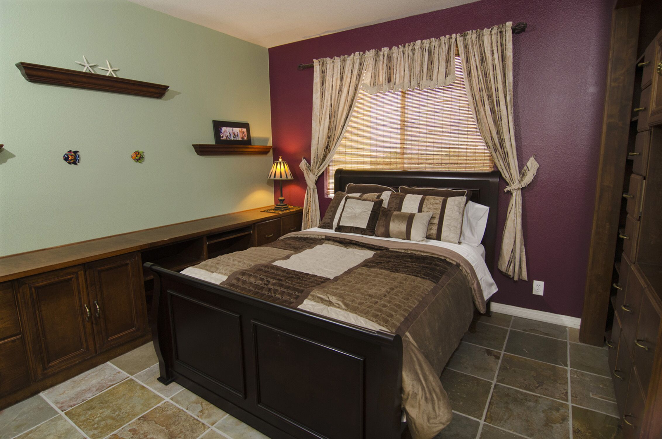 A bedroom with a bed, a nightstand, a dresser, and a window with curtains.