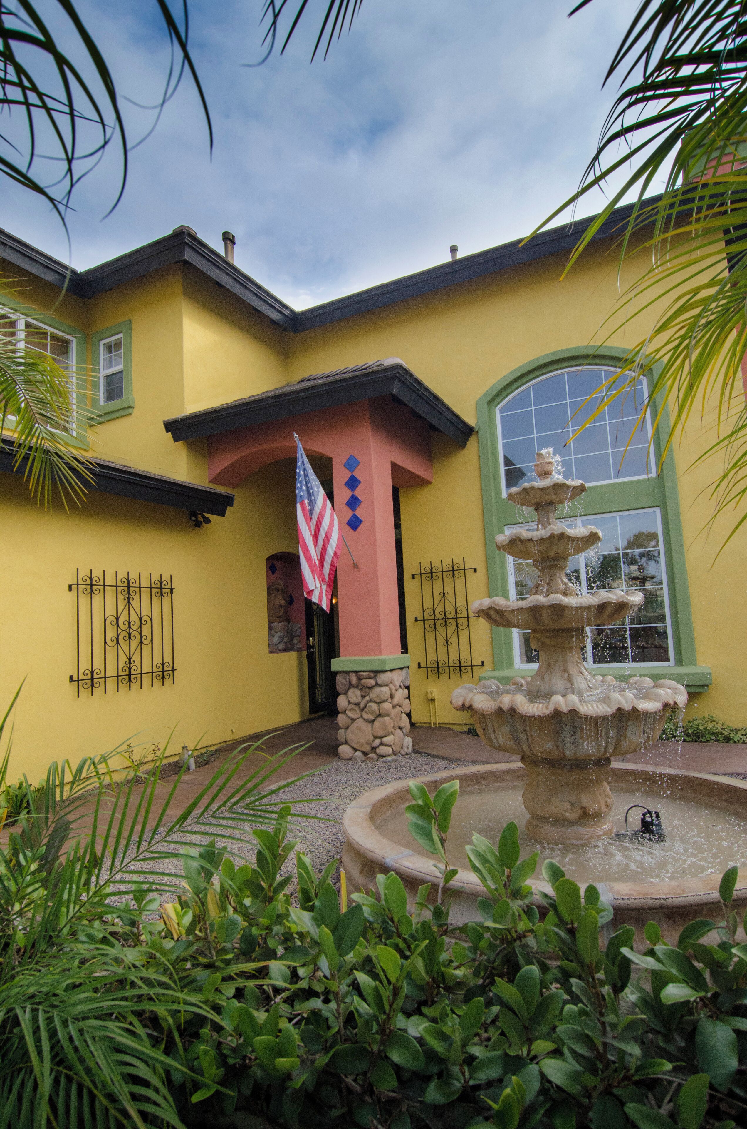 A yellow building with a stone fountain and an American flag.