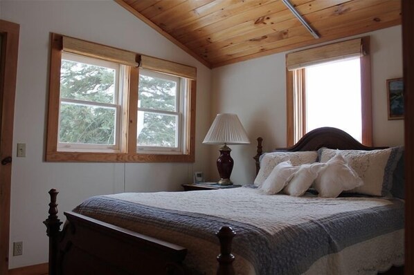 Classic bedroom with a wooden bed, bedside lamp, and two windows.