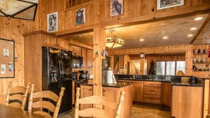 A wooden cabin-style kitchen with a dining area, featuring a refrigerator, stove, and wooden chairs.