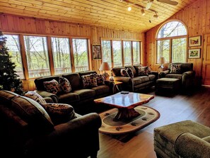 Interior acogedor de una cabaña con paredes de madera, ventanas amplias, chimenea y un árbol de Navidad.