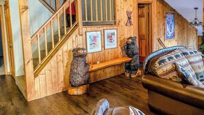 A wooden interior with a staircase, a bench, two bear sculptures, and a couch.