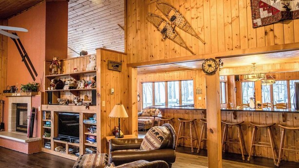 A cozy lodge interior with a fireplace, leather seating, wooden walls, and a bar area.