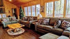 A cozy cabin interior with wooden walls, large windows, and a fireplace.