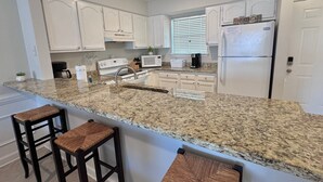 Una cocina moderna con armarios blancos, encimeras de granito, un refrigerador de acero inoxidable y dos taburetes de bar.