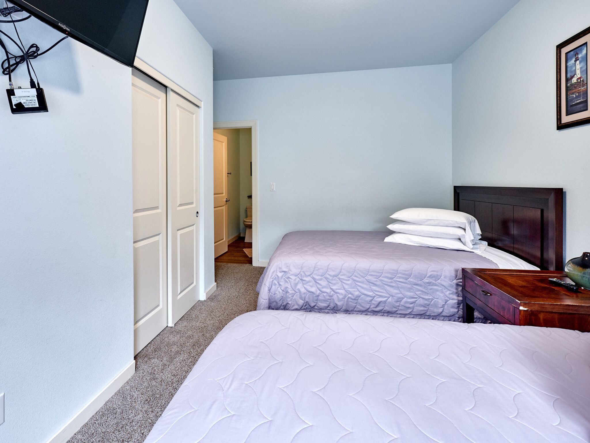 A bedroom with two beds, a wooden headboard, a bedside table with a lamp, and a framed picture on the wall.