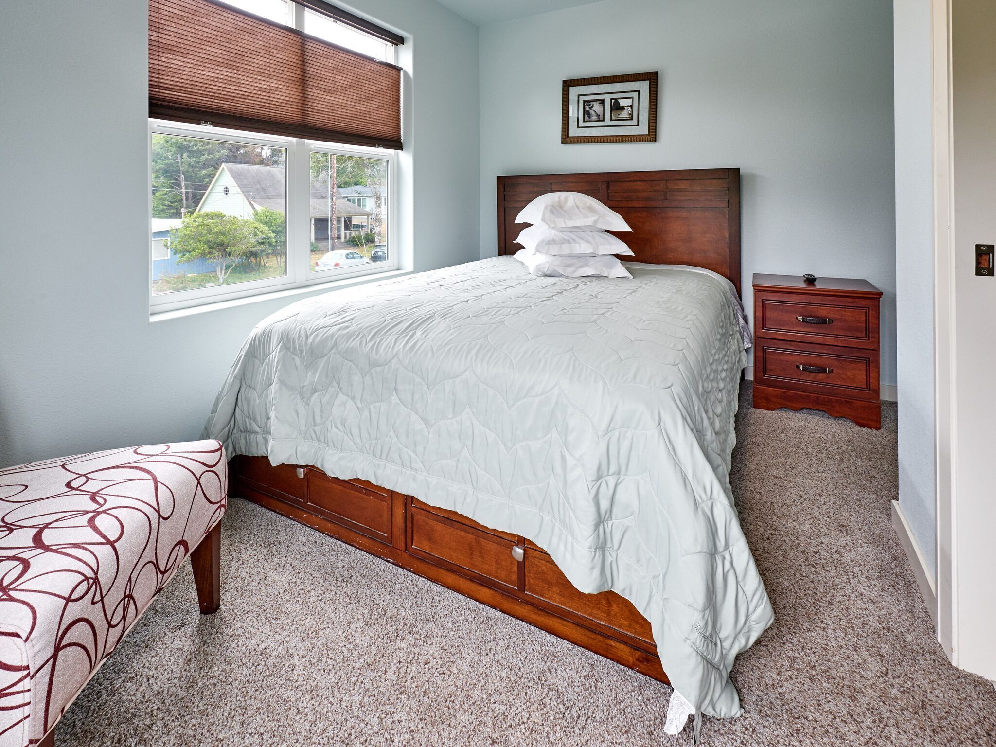 A bedroom with a bed, a nightstand, a dresser, a window with blinds, and a picture on the wall.