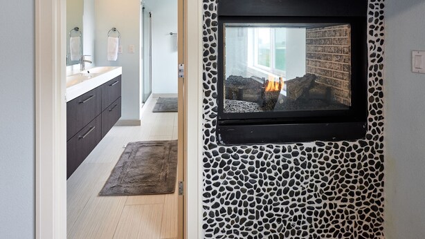 Une salle de bain moderne avec un mur décoré d’un motif imitant la pierre, un téléviseur fixé au mur et une cheminée bien visible.