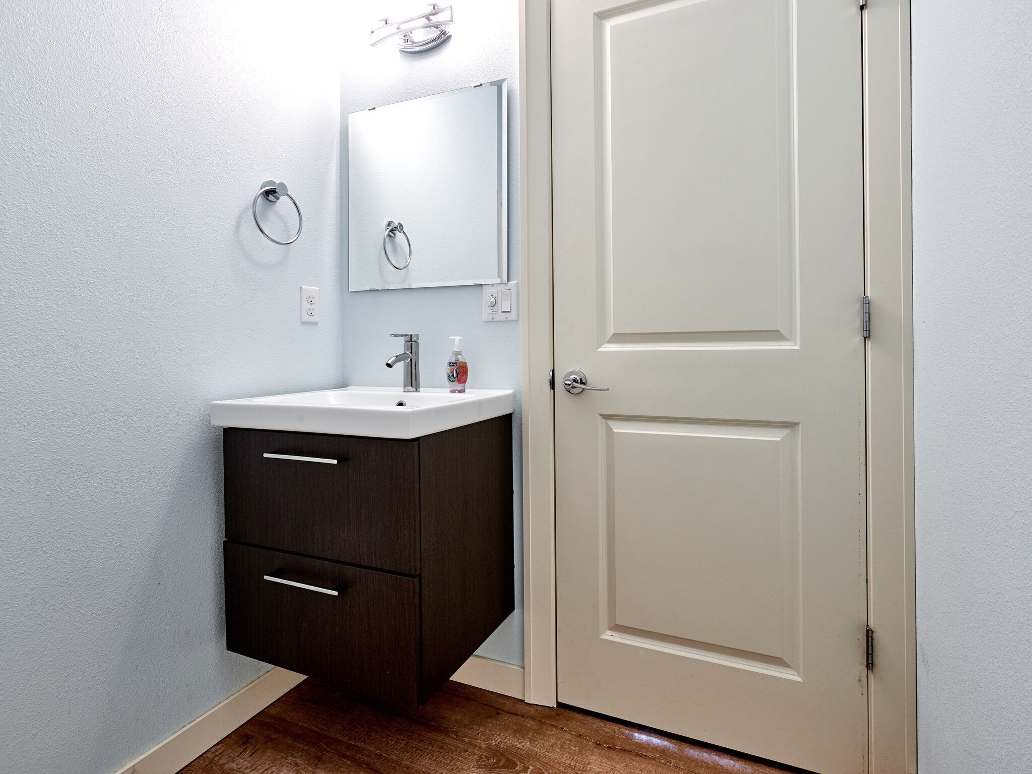 Une salle de bain avec un lavabo blanc, un meuble sombre et une porte.