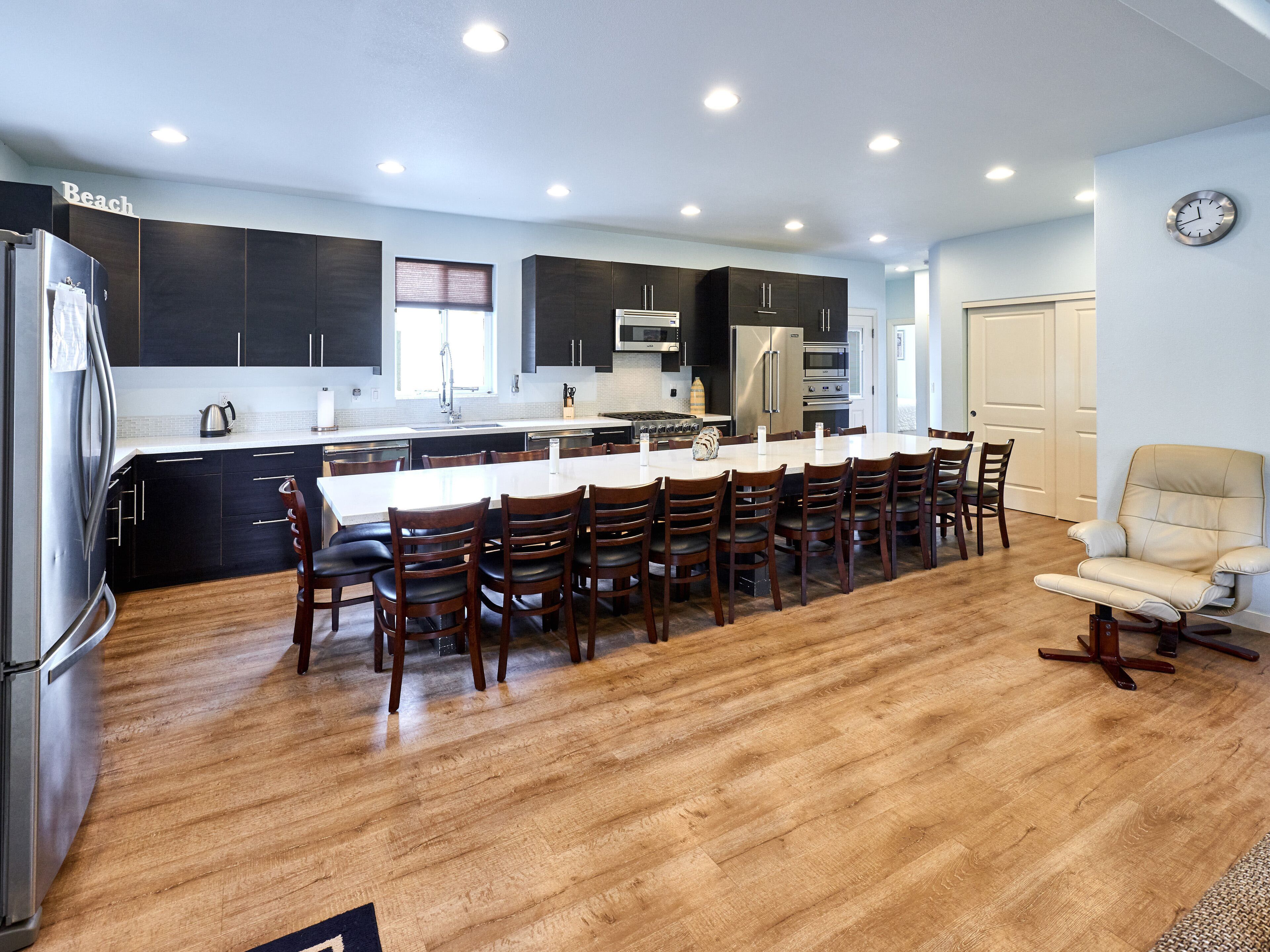 A modern kitchen with dark cabinets, a large island, and a dining area with wooden chairs.