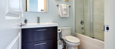 Un bagno moderno con lavandino bianco, mobile contenitore scuro, water e box doccia in vetro.