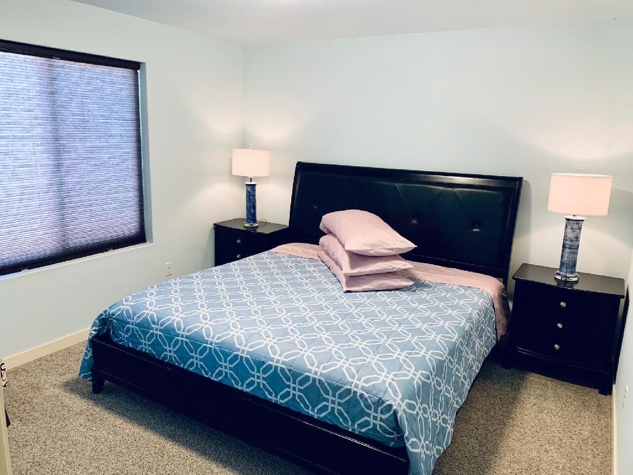 A bedroom with a bed, two nightstands, a window with blinds, and a lamp on each nightstand.